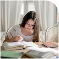A student writing in a notebook while studying at a desk.