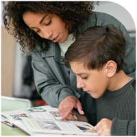 A mentor sitting beside a student, helping him work through a book.