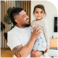 A father lifting his young daughter up, both smiling.